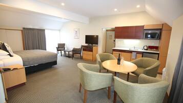 A hotel room with a bed, a desk, a television, a microwave, and a dining area with chairs.
