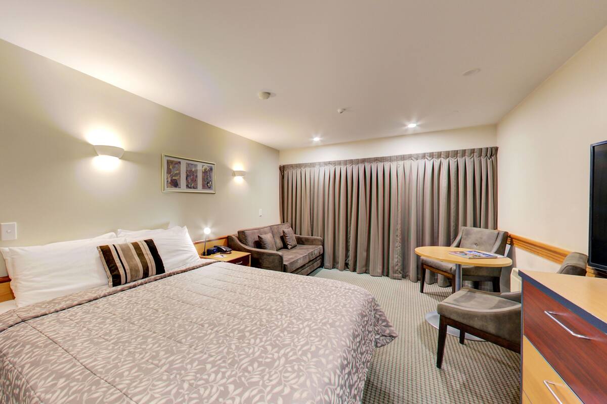 A hotel room with a large bed, a desk with a chair, a television, and a window with curtains.