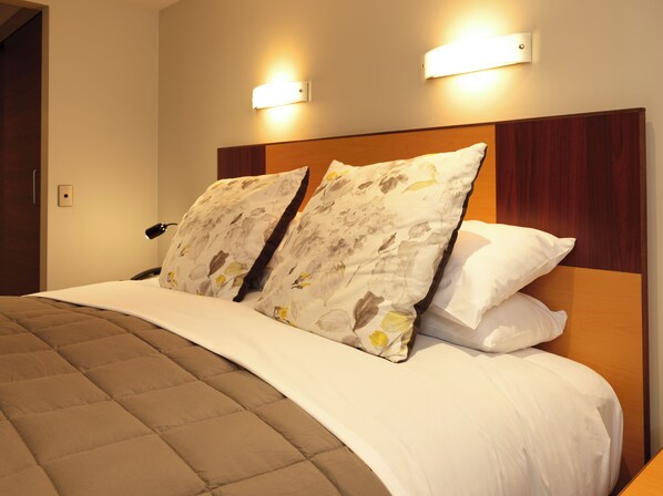 A neatly made bed with a brown quilt, two floral pillows, and a wooden headboard. - Dunedin Leisure Lodge - A Distinction Hotel (Dunedin)