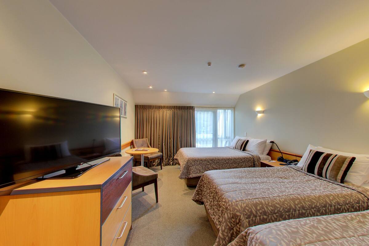 A hotel room with two beds, a TV, a desk, and a chair.