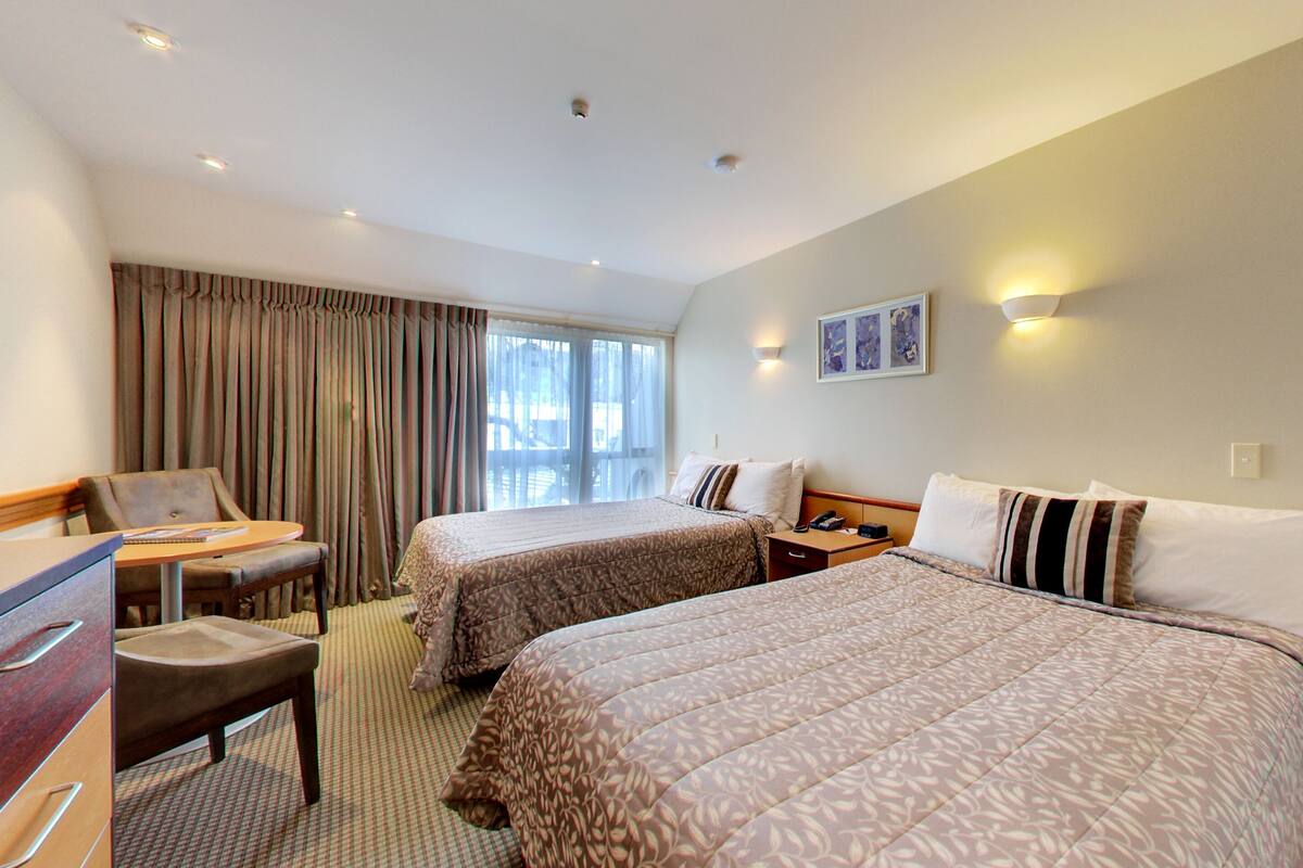 A hotel room with two beds, a desk, a chair, and a window with curtains.