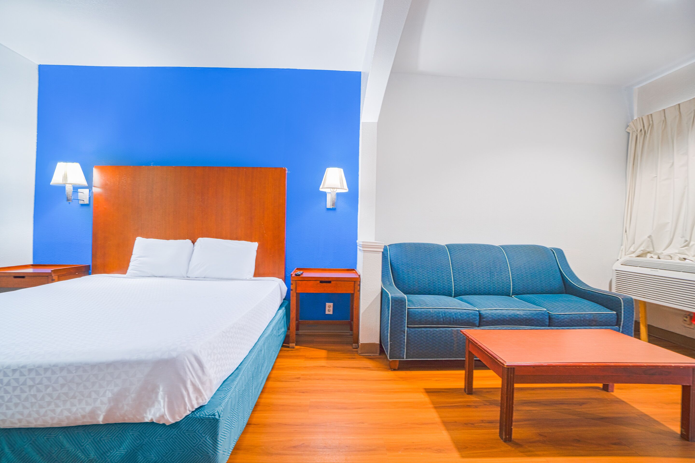A hotel room with a bed, a blue armchair, a wooden nightstand, and a table.