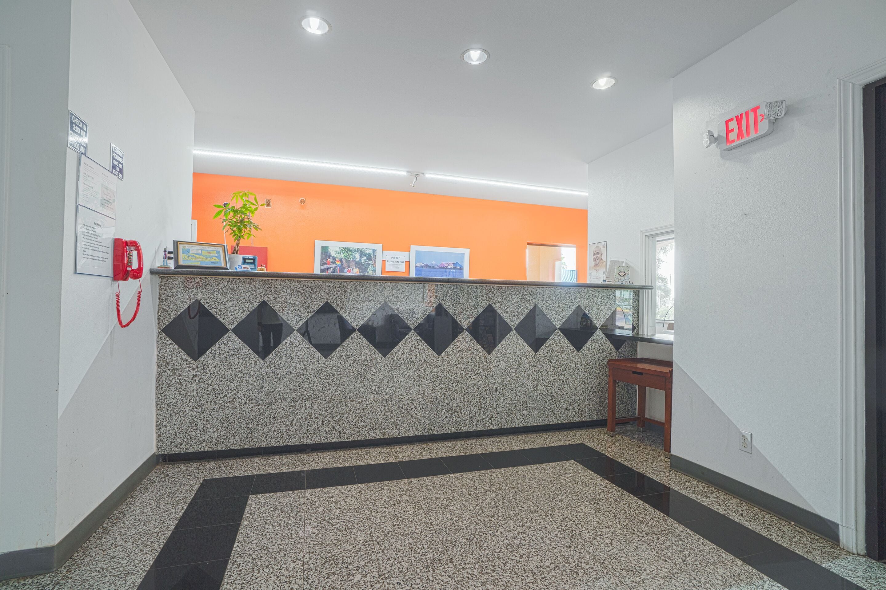 A reception area with a counter, a red phone, framed pictures, and an exit sign.