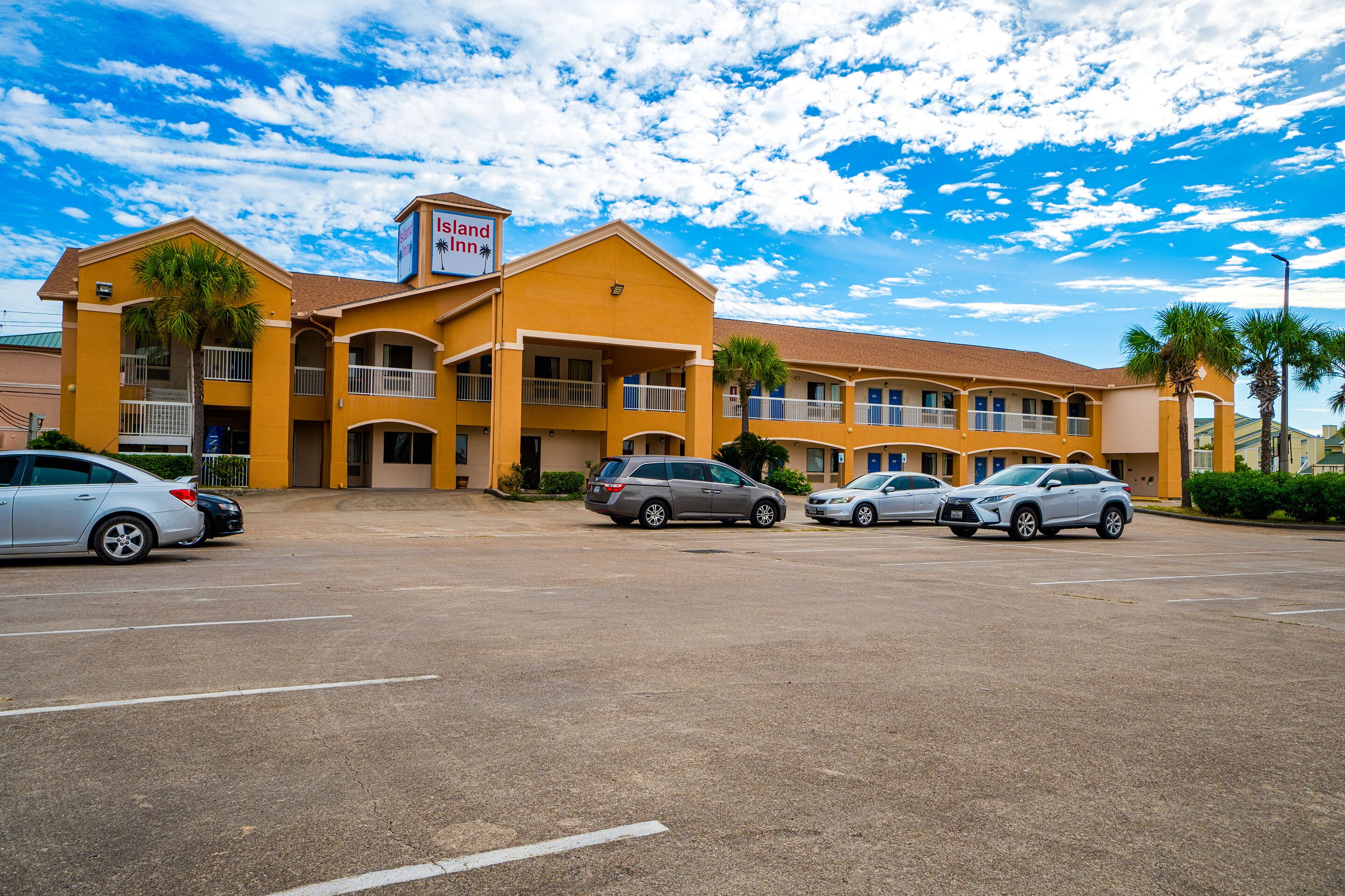 A motel with multiple parking spaces and a clear blue sky with clouds.