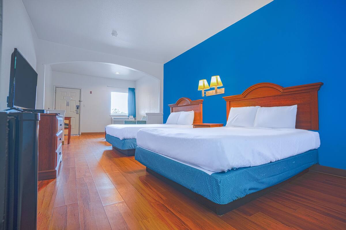 Une chambre d’hôtel avec deux lits, un plancher en bois, une télévision et un bureau.