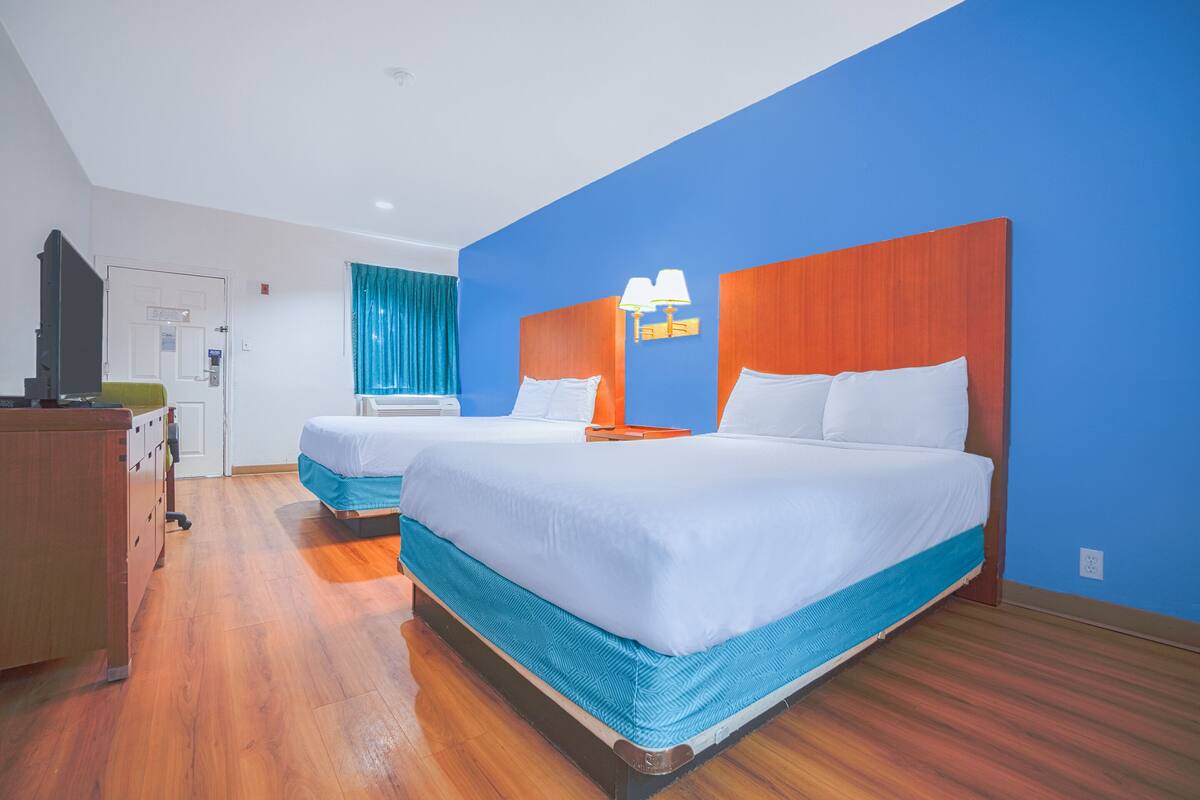 Une chambre d’hôtel avec deux lits, un plancher en bois, une télévision et un bureau.