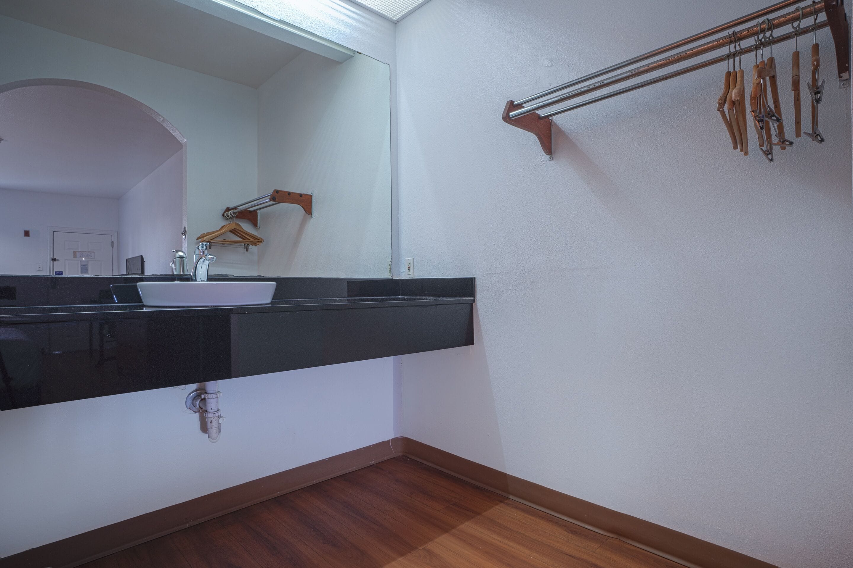 Un baño con encimera negra, lavabo blanco y espejo. Hay un perchero con toallas de madera y un toallero de madera en la pared.