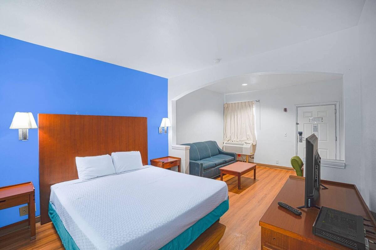 Une chambre d’hôtel avec un grand lit, un bureau avec un ordinateur, une chaise, une télévision et une fenêtre avec des rideaux.