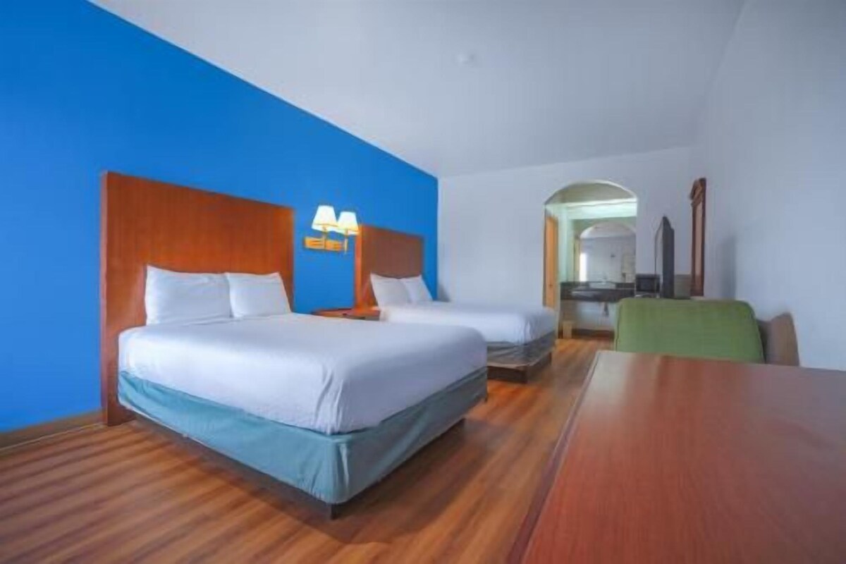 Een hotelkamer met twee bedden, een houten vloer, een blauwe wand en een eettafel.