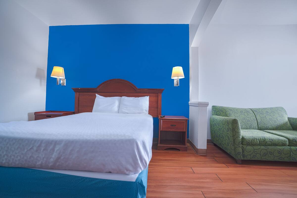 Une chambre d’hôtel avec un grand lit, deux lampes de chevet, un canapé vert et un plancher en bois.