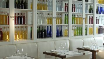 Un interior de restaurante con cabinas blancas, mesas con manteles blancos y estantes con varias botellas.