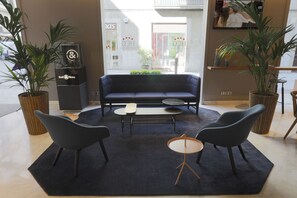 Un área de estar moderna con un sofá azul oscuro, dos sillones negros, una mesita redonda y plantas en macetas.