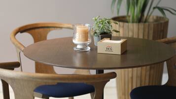 Una mesa de madera redonda con una vela, una pequeña planta en maceta y una caja etiquetada como 'HCG Hotel Cortez de Guatemala'.