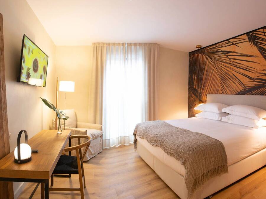 Habitación de hotel con cama, mesita de noche, lámpara y televisor montado en la pared.
