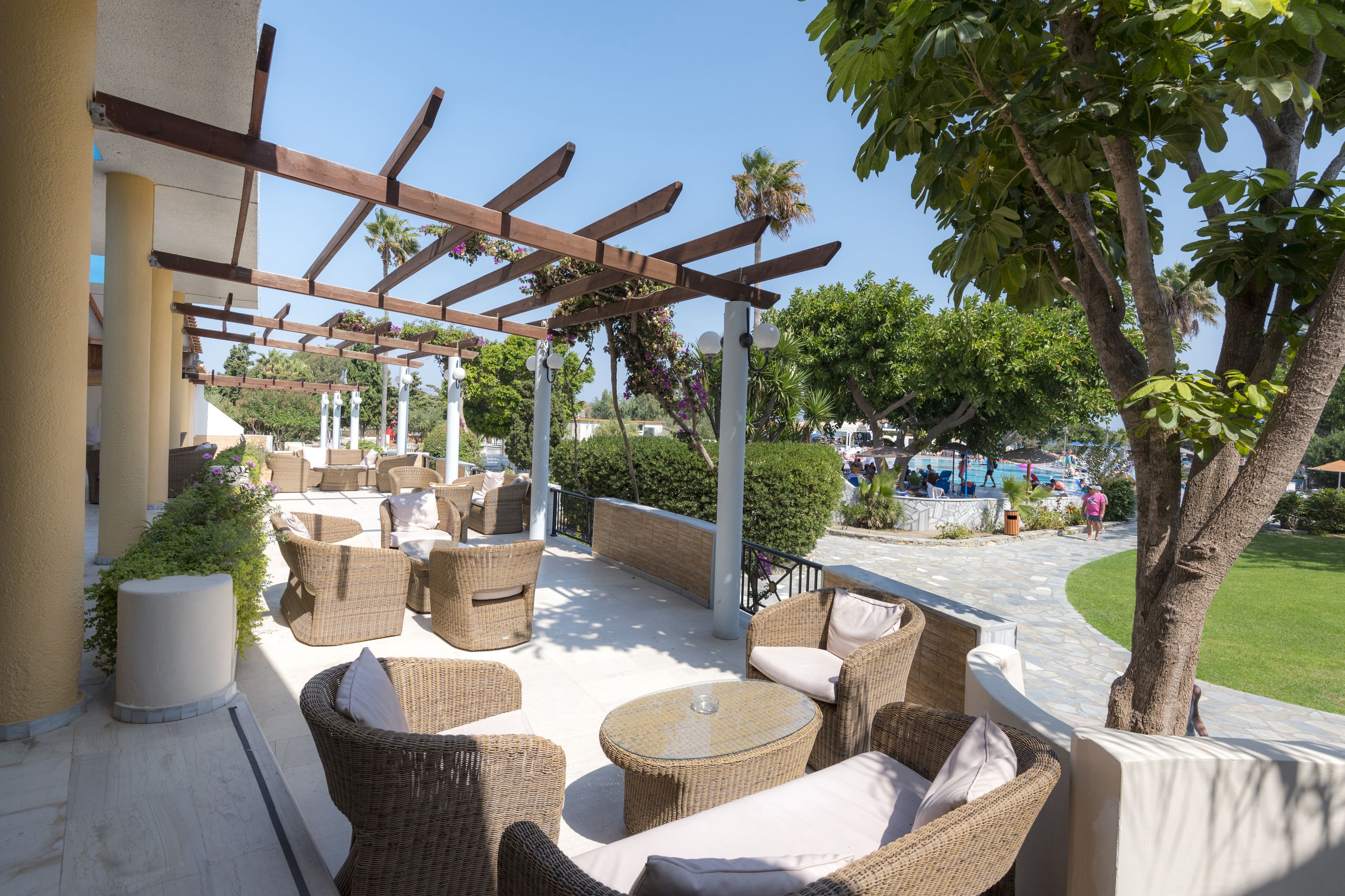 An outdoor patio with wicker furniture, a pergola, and a view of a pool area.