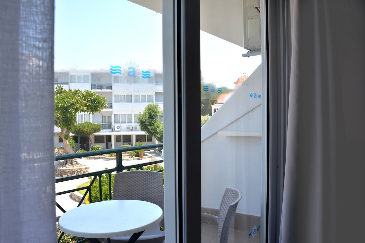 A balcony with a table and chair, overlooking a building with a blue logo.