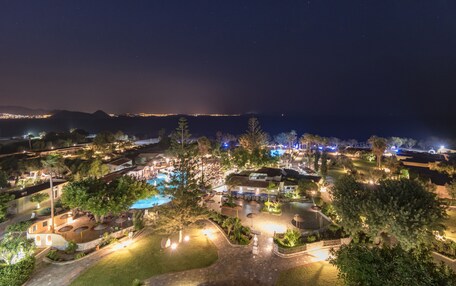 An aerial view of a resort with a swimming pool, outdoor seating areas, and a well-lit landscape at night.