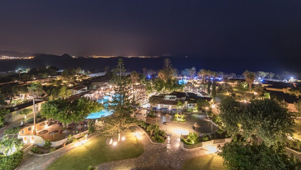 Vista aérea de un resort con piscina, zonas de estar al aire libre y un paisaje bien iluminado durante la noche.