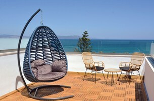A balcony with a hanging chair, two wicker chairs, and a small round table.
