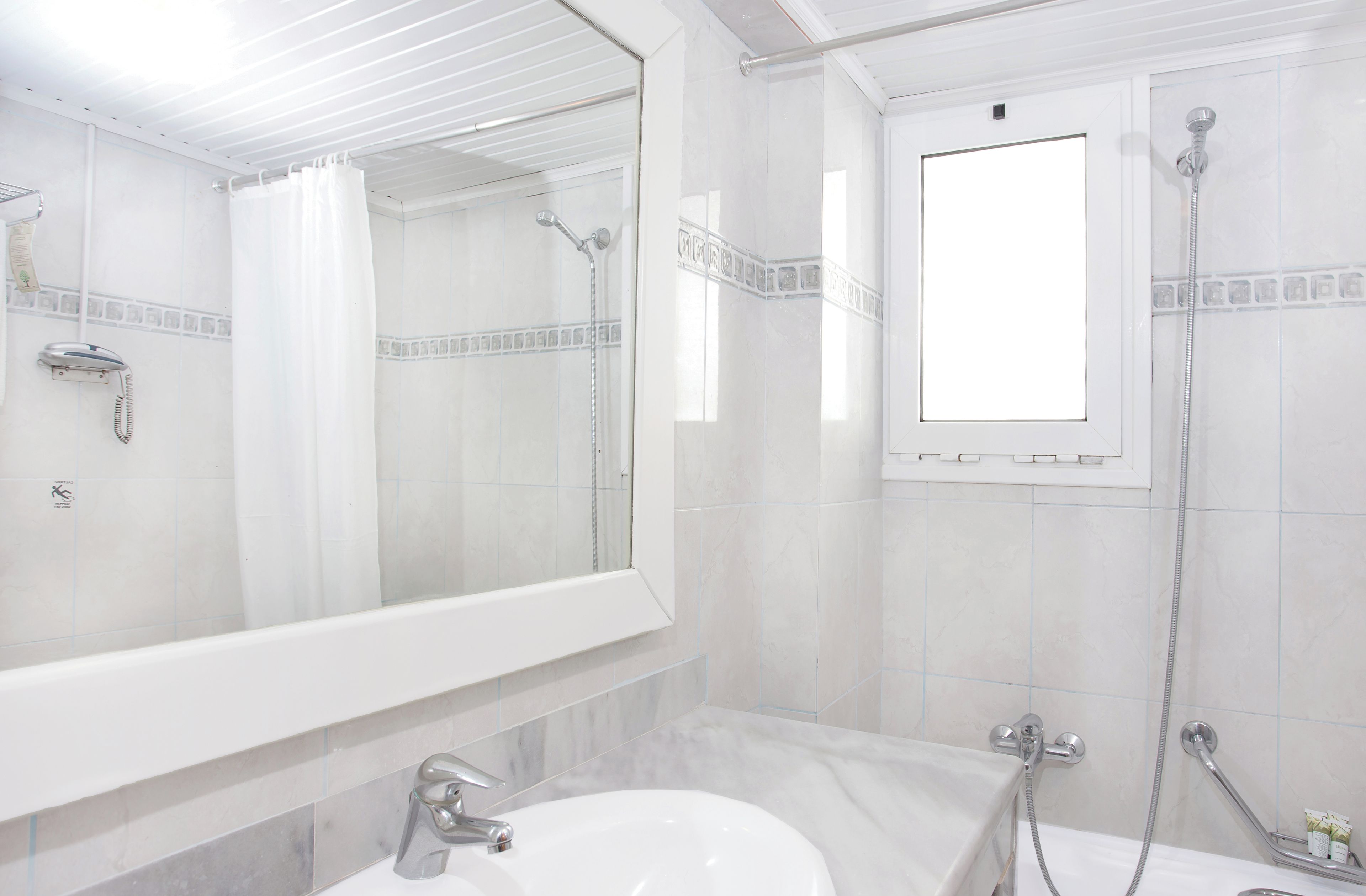 A bathroom with a large mirror, a shower, a sink, and a window.