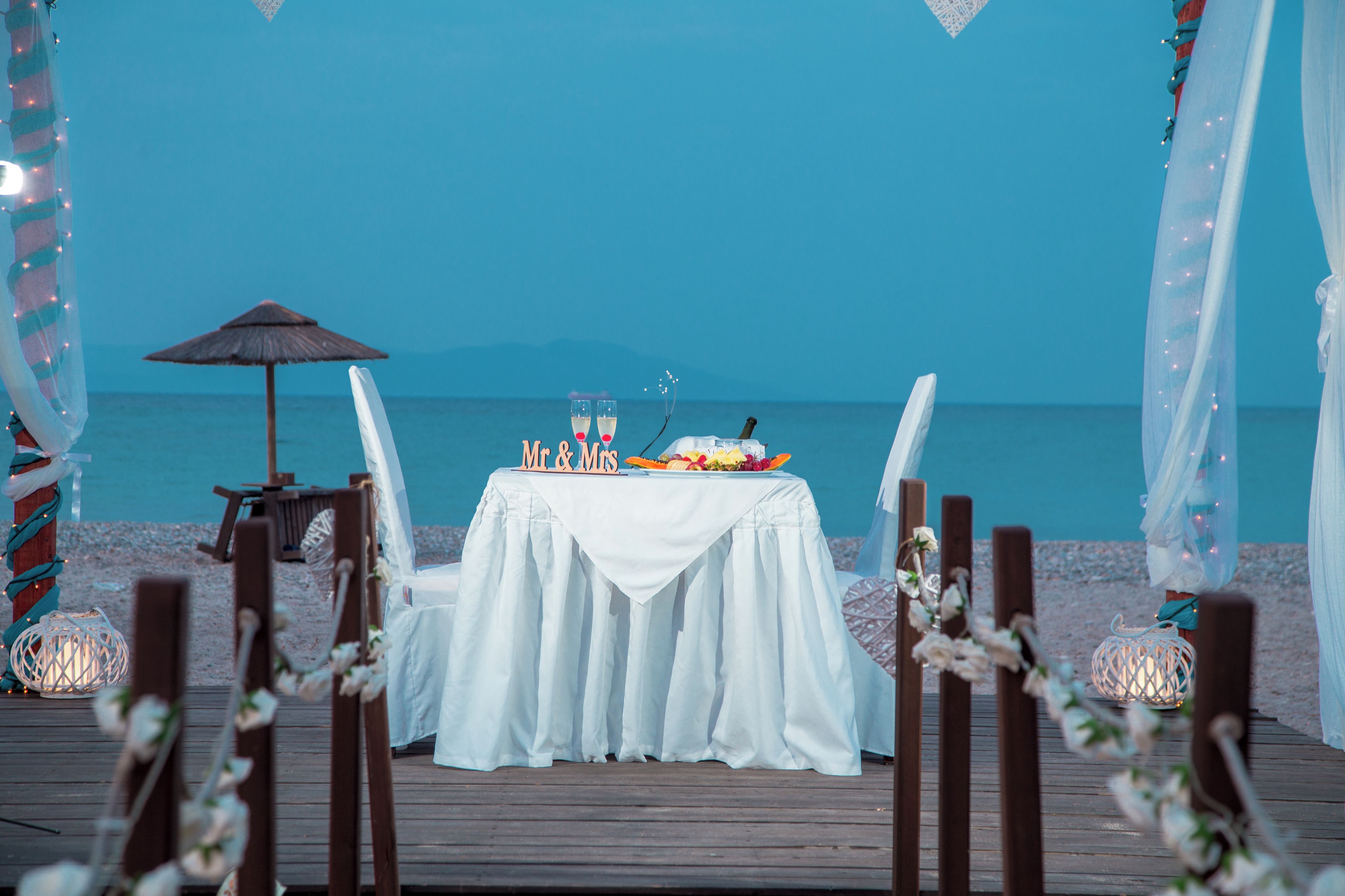 A beachside dining setup with a table, chairs, and a view of the sea.