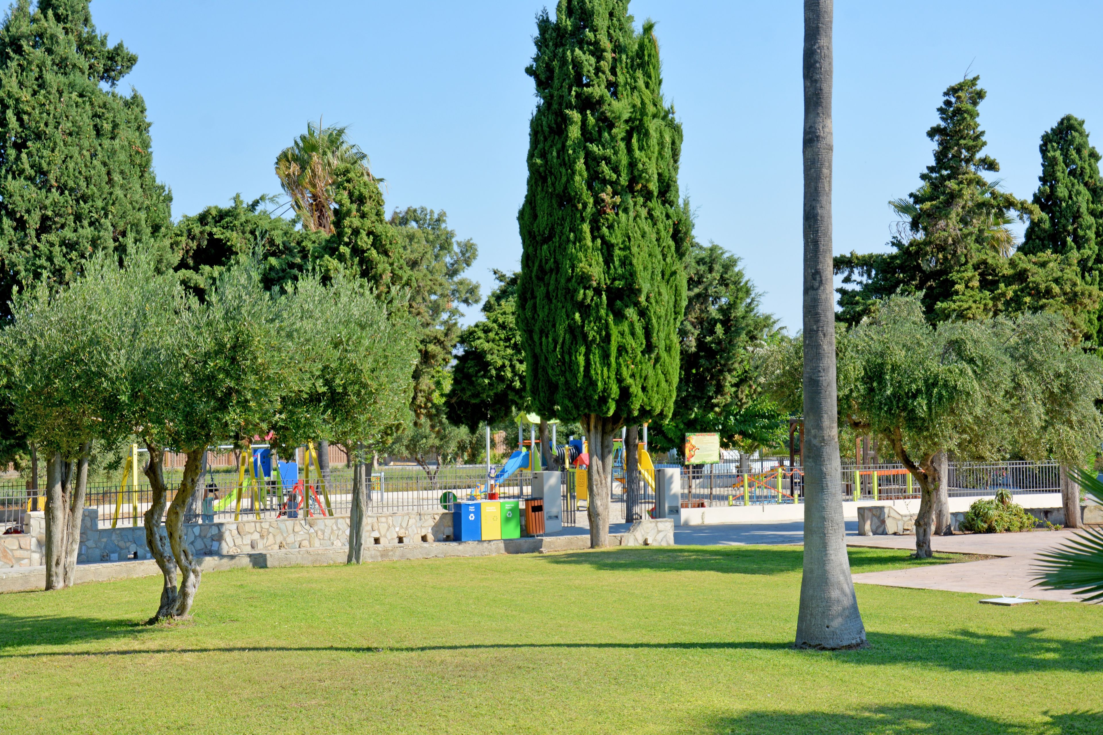 Ein Park mit Spielgeräten, einer Steinmauer und Bäumen.