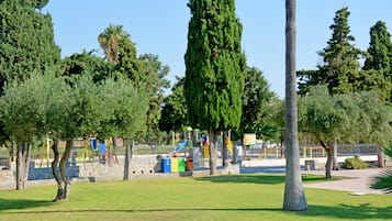 Ein Park mit Spielgeräten, einer Steinmauer und Bäumen.