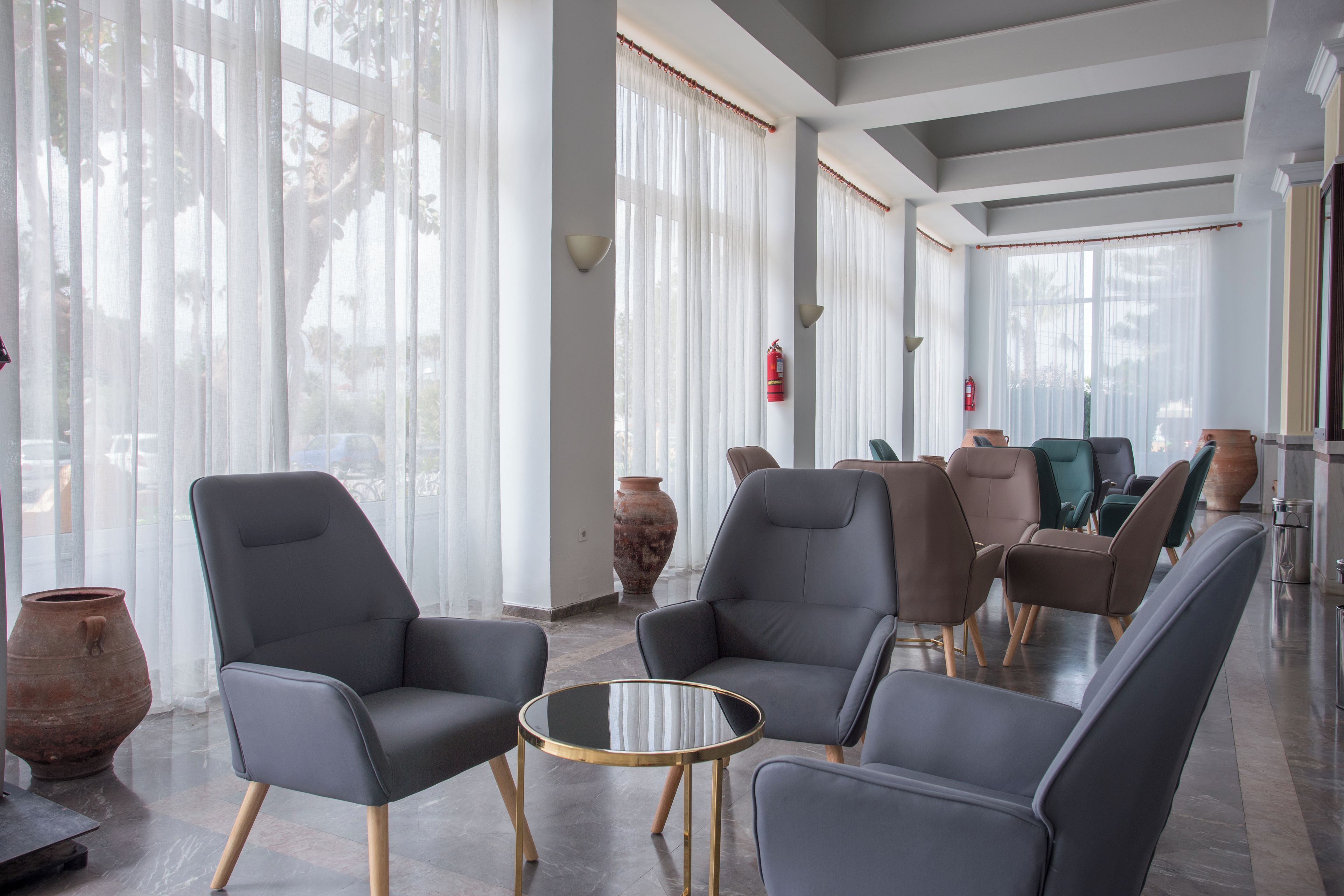 Eine moderne Lounge mit Ledersesseln, einem Glastisch und großen Fenstern mit transparenten Vorhängen.