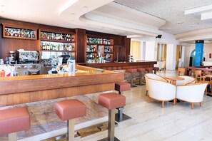 Una zona de bar con mostrador de madera, varias estanterías llenas de botellas y asientos con taburetes acolchados.