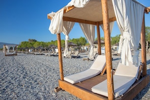Un entorno frente al mar con una cama con dosel de madera, sillones de descanso y sombrillas.
