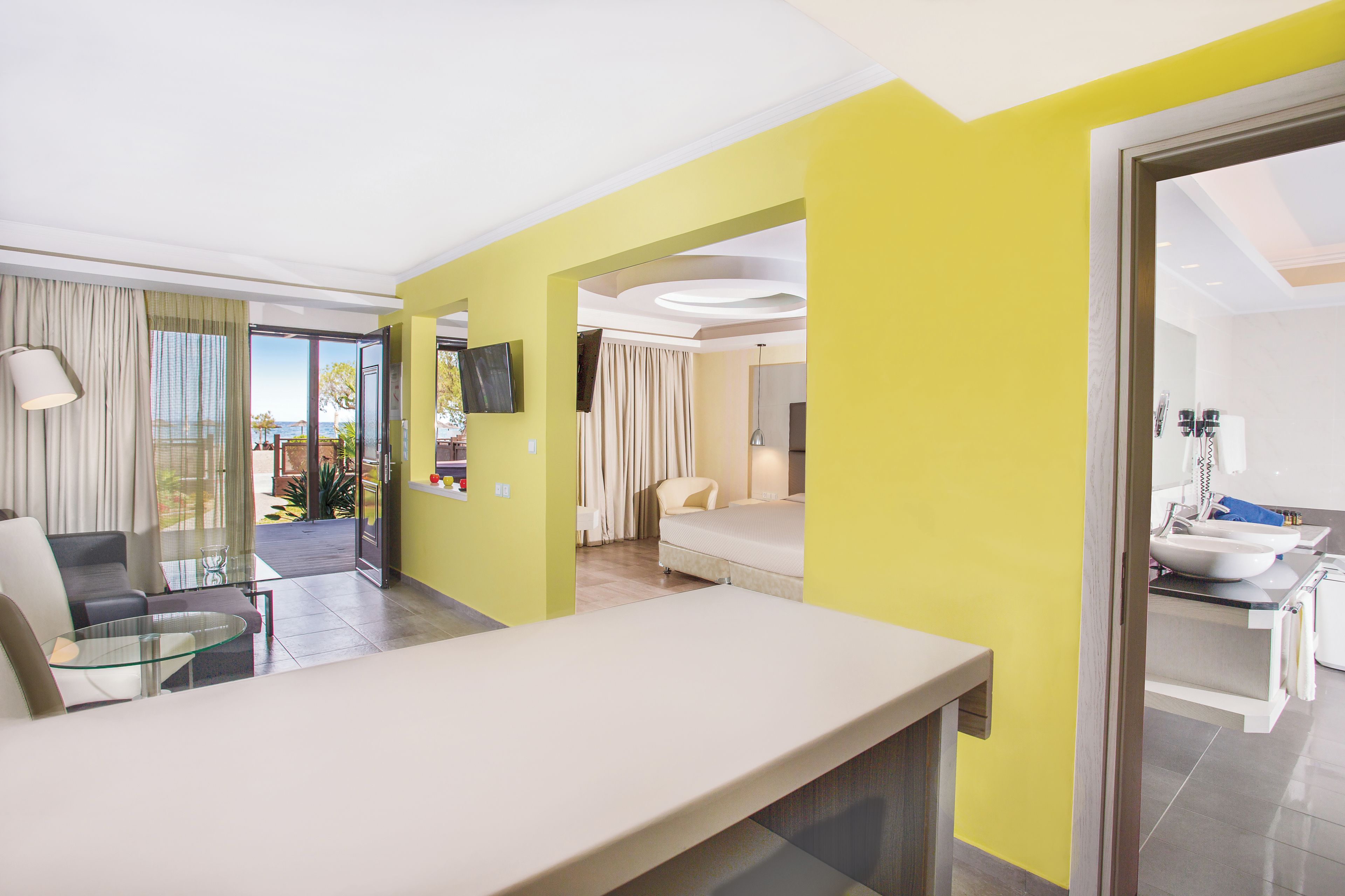 Une chambre d’hôtel dotée d’un grand lit, d’un coin salon avec une table et des chaises, d’un téléviseur fixé au mur et d’une salle de bain avec un lavabo et un miroir.