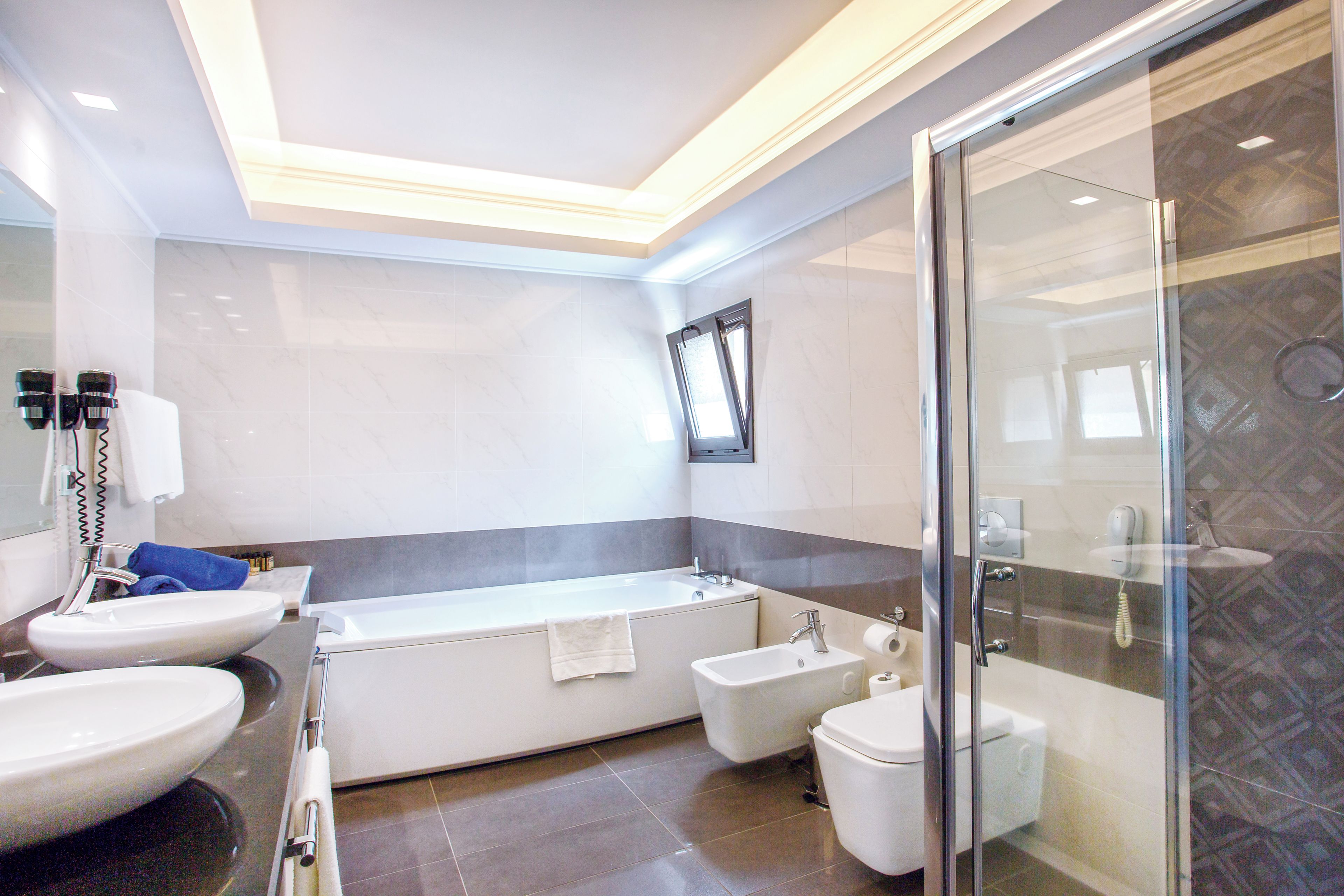 Un baño moderno con bañera, dos lavamanos, inodoro y cabina de ducha de vidrio.