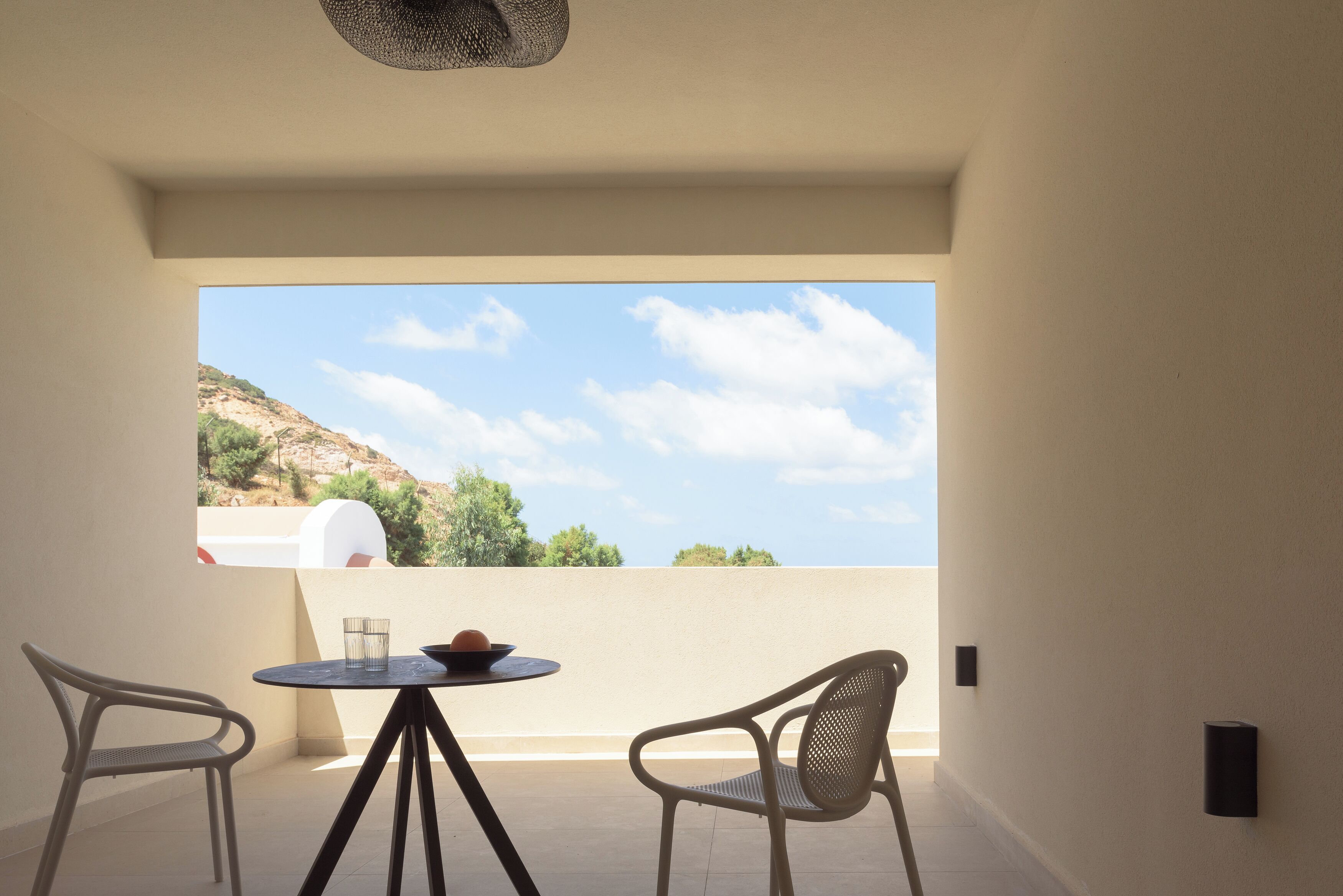 A balcony with two chairs, a table, and a view of a mountainous landscape.