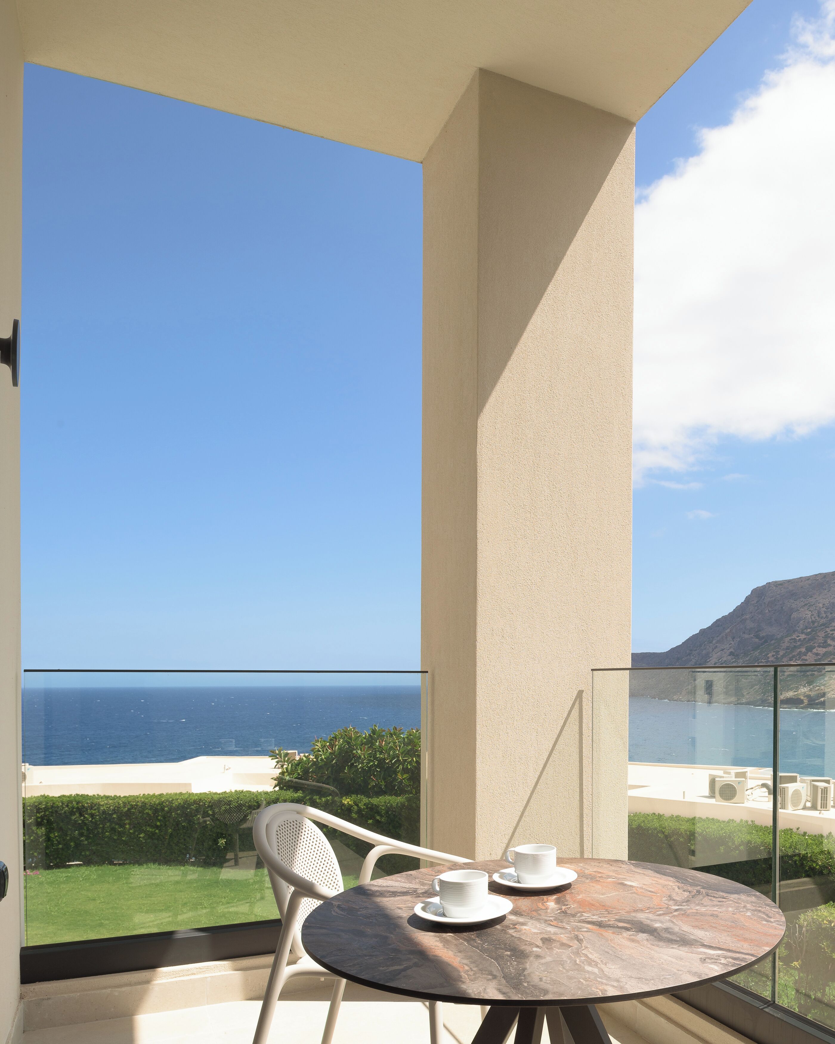 Un balcon avec une table et des chaises, offrant une vue sur la côte, avec la mer et une montagne en arrière-plan.