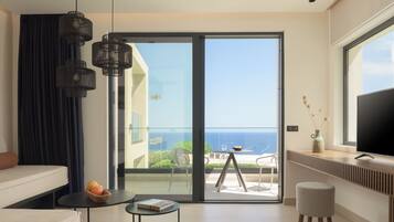 Una sala de estar moderna con un sofá, una mesita con un libro y fruta, un televisor y un balcón con vista al mar.