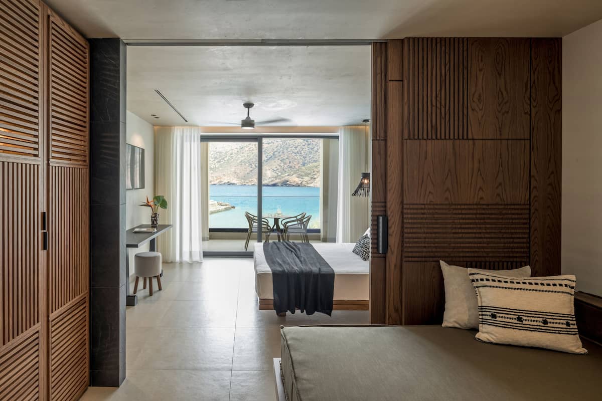 A modern hotel room with a bed, a desk, and a view of the sea.