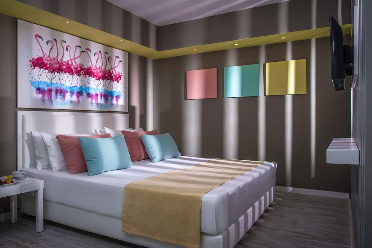 A modern bedroom with a large bed, a bedside table, a wall-mounted TV, and a colorful abstract painting.