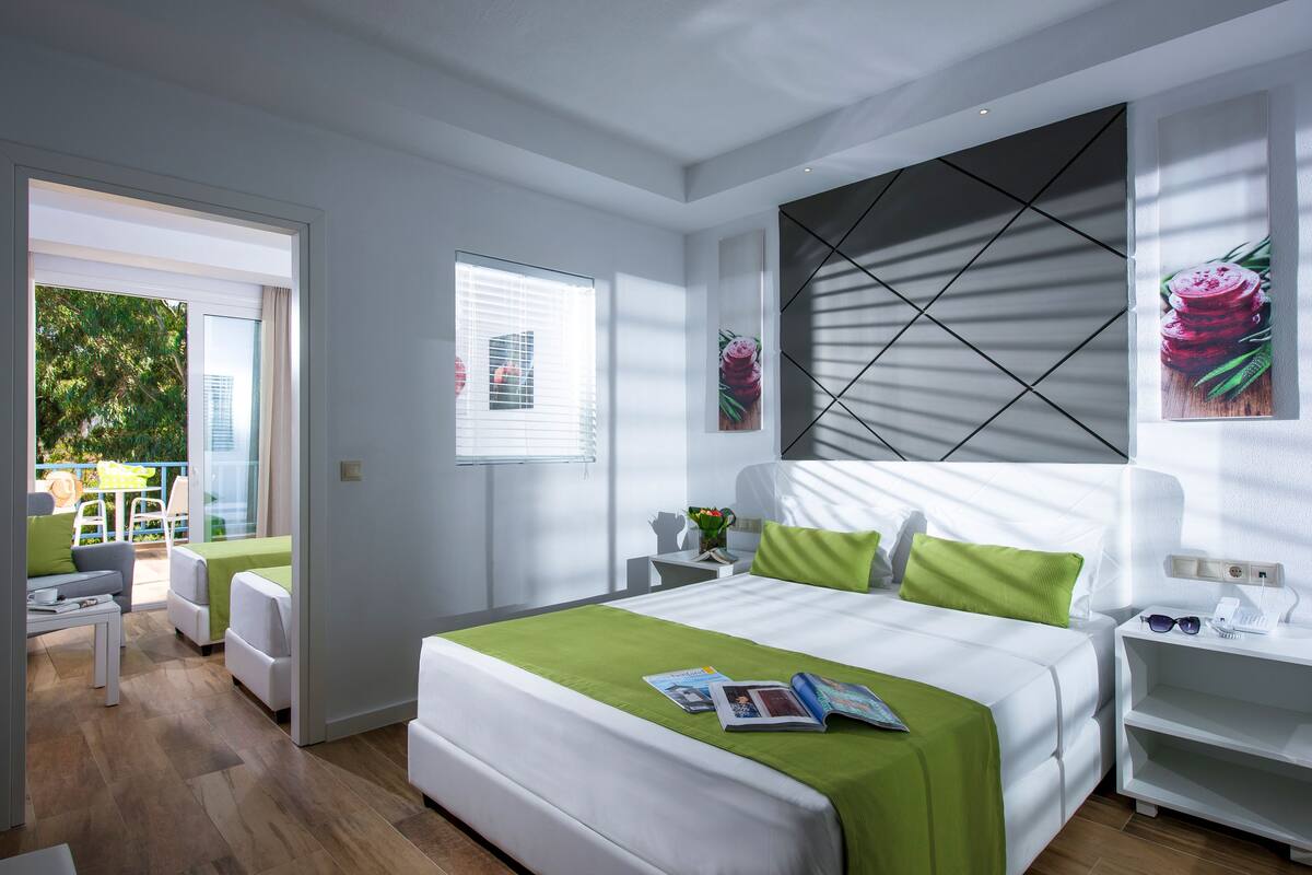 A modern hotel room with a large bed, a green accent wall, and a view of the outdoors.