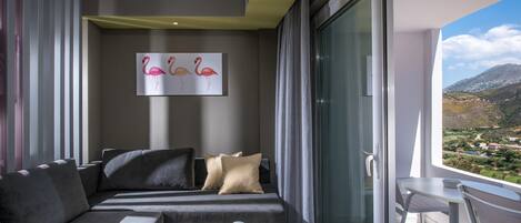 A modern hotel room with a sofa, a dining table with a plate of food, and a painting of flamingos on the wall.
