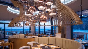 A modern restaurant with a curved seating area, wooden furniture, and a unique ceiling light fixture. - Fodele Beach & Water Park Holiday Resort - All Inclusive (Malevizi)
