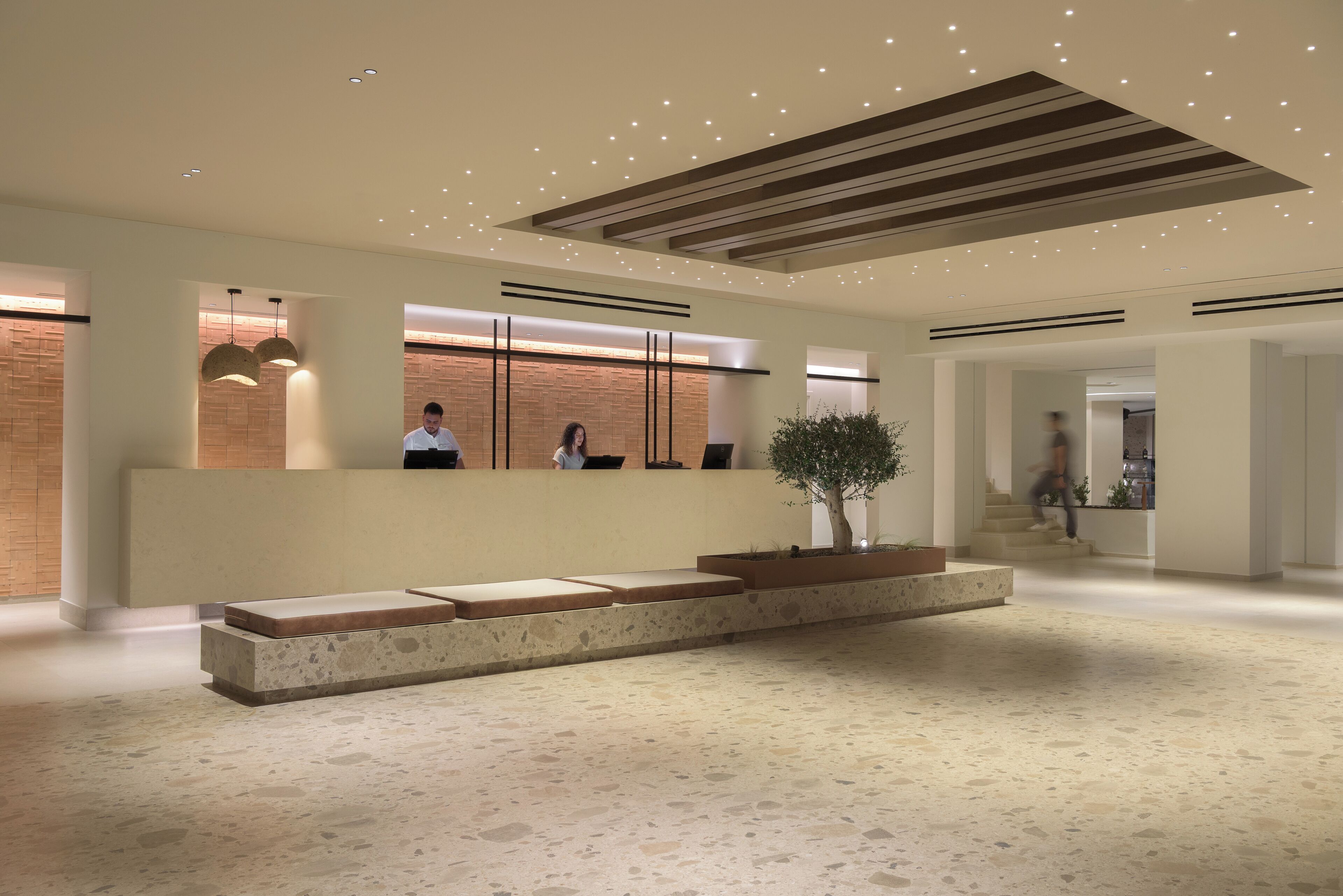 Un área de recepción moderna con mostrador, zona de estar y una escalera que sube a los pisos superiores.