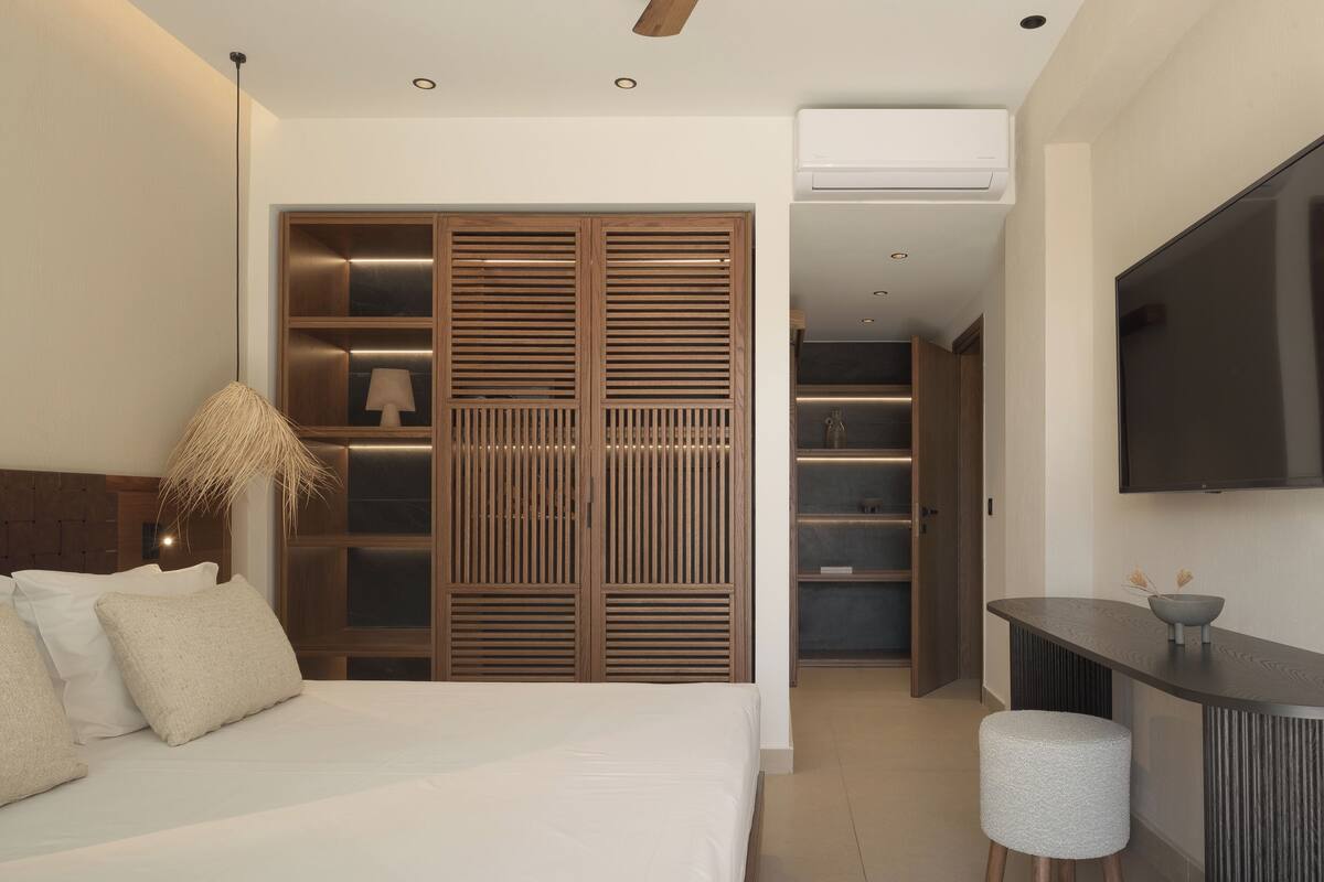 A modern bedroom with a bed, bedside lamp, wardrobe, and a small seating area with a table and ottoman.