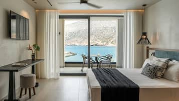 A modern hotel room with a bed, a desk, a chair, and a view of the sea.