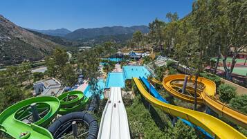 Parque acuático con varias toboganes y una piscina, rodeado de montañas y árboles.