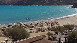 A beach with numerous sun loungers and umbrellas, a flag, and a mountainous backdrop. - Fodele Beach & Water Park Holiday Resort - All Inclusive (Malevizi)