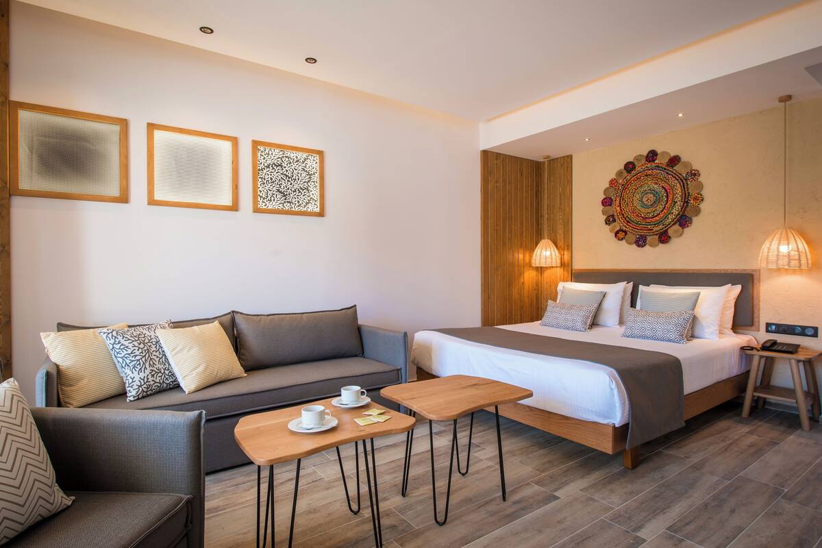 A modern hotel room with a sofa, a bed, a small table, and a decorative wall piece.