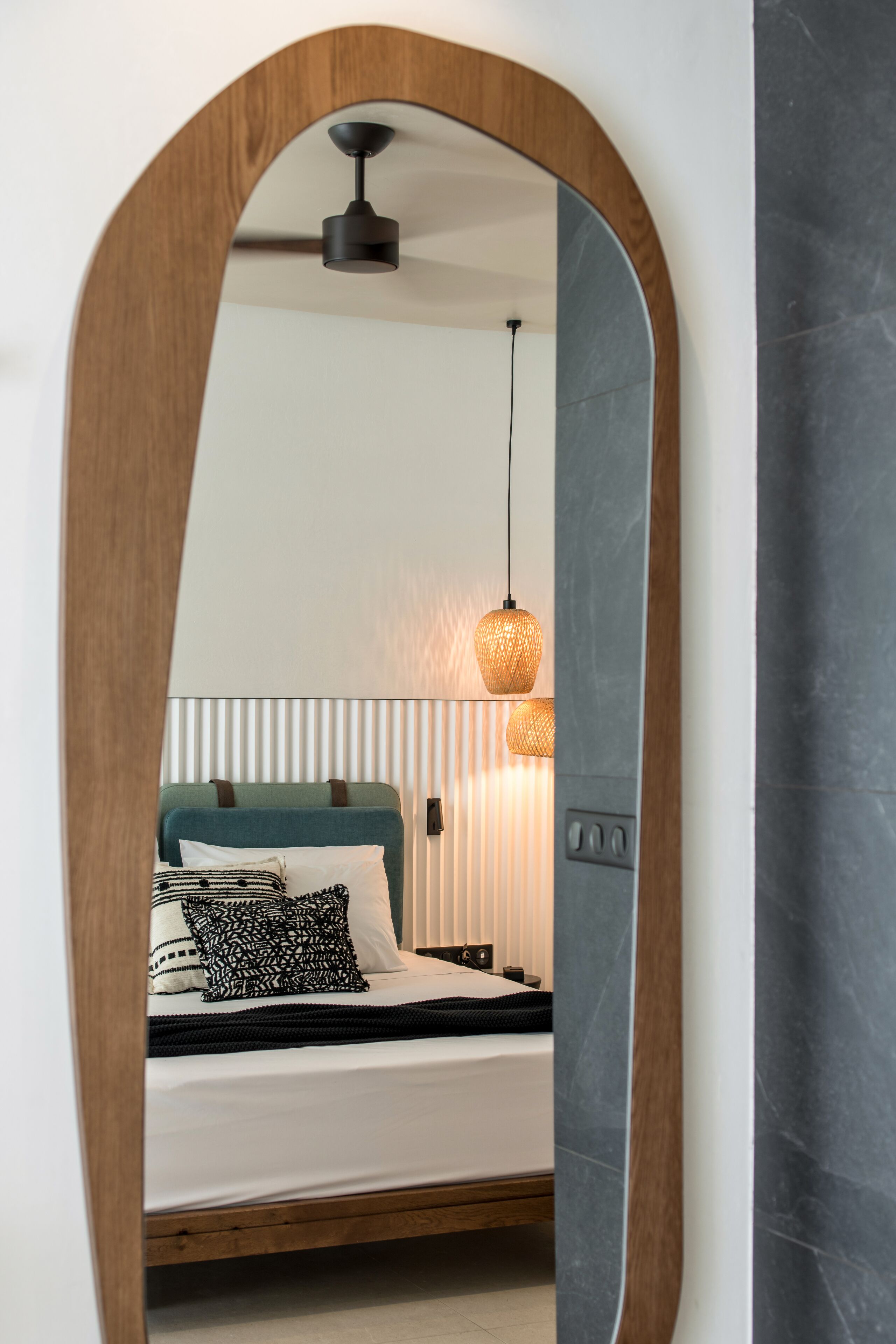A bedroom with a bed, a hanging light fixture, and a wooden-framed mirror.