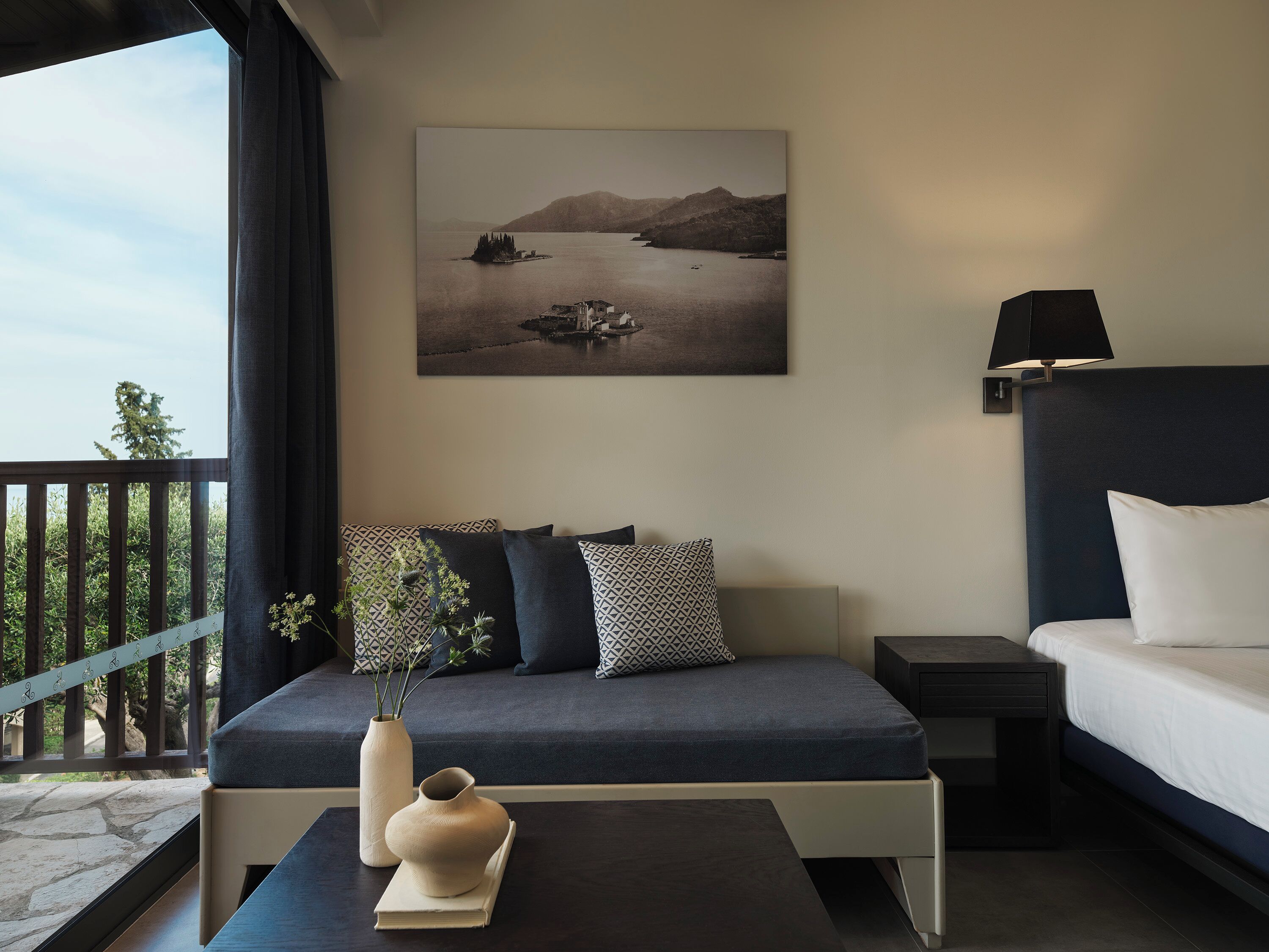 A modern bedroom with a bed, bedside table, and a painting of a lake.