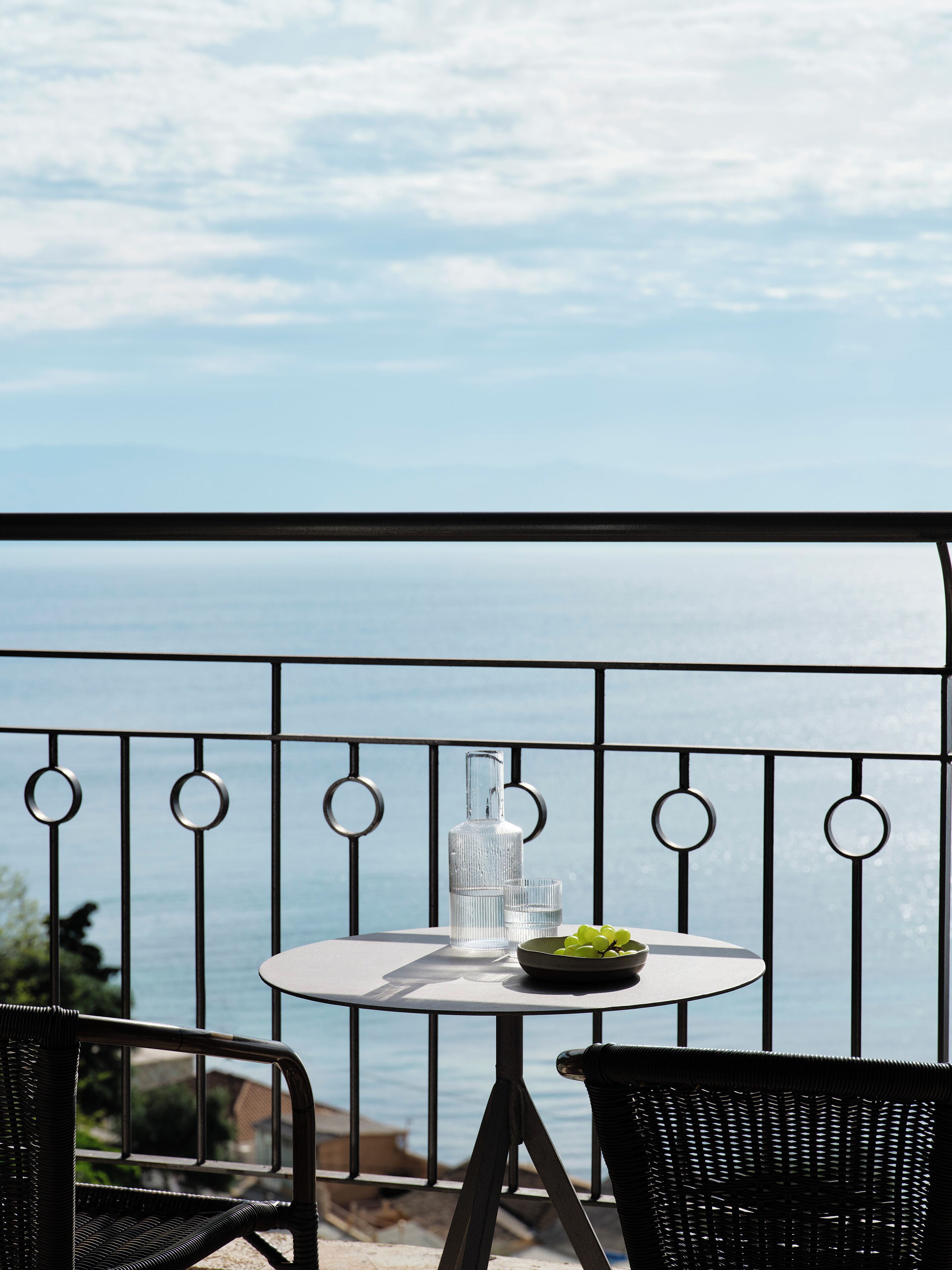 A round table with a bottle and glasses on a balcony overlooking the sea.