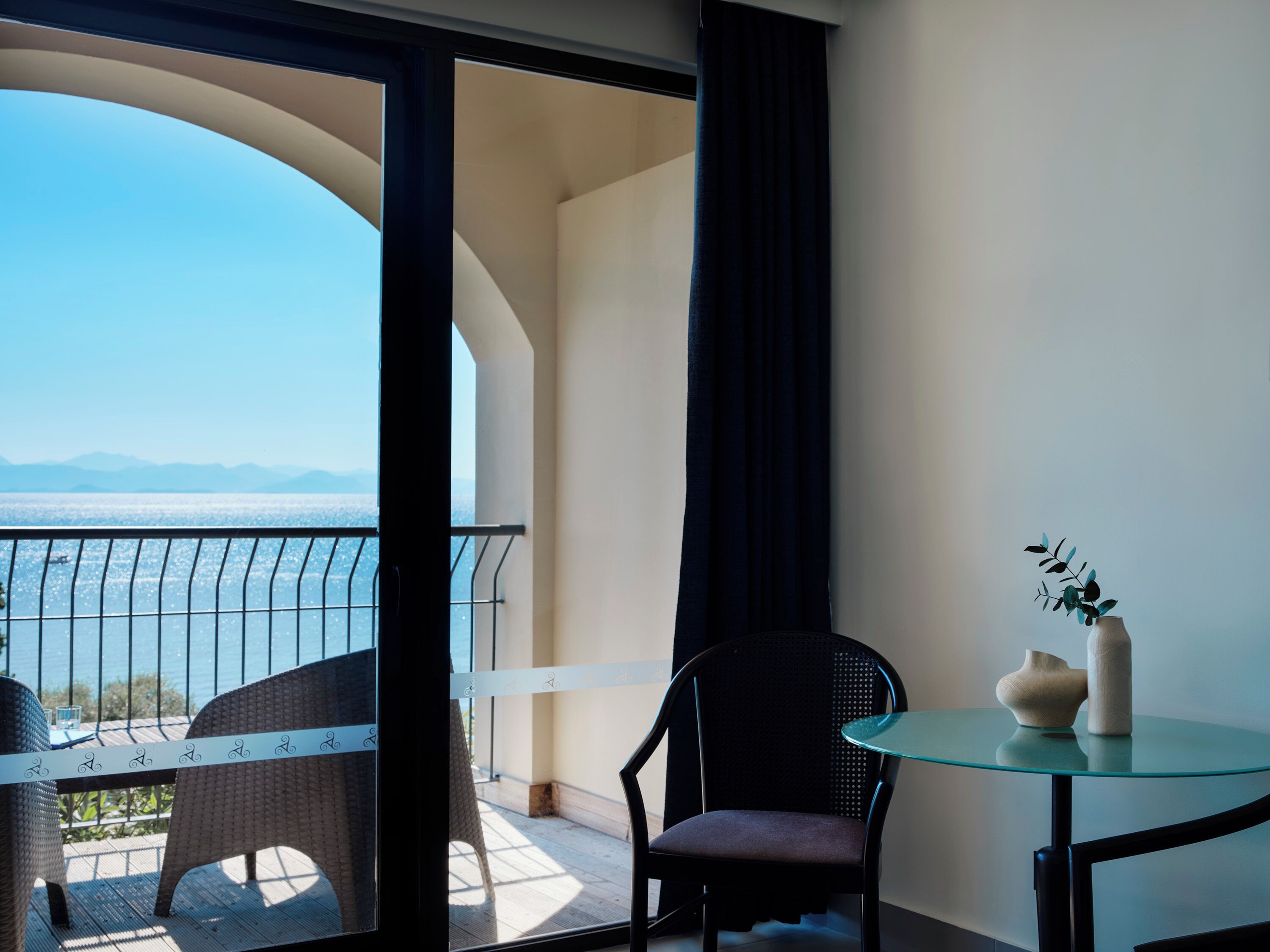 A balcony with wicker chairs, a glass table, and a vase with a plant.